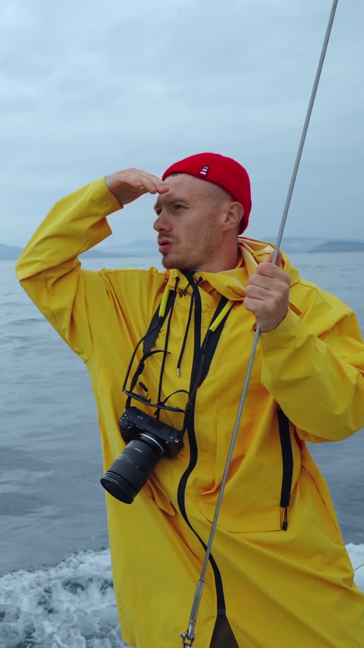 Mann i gul regnjakke ser ut over havet fra en båt