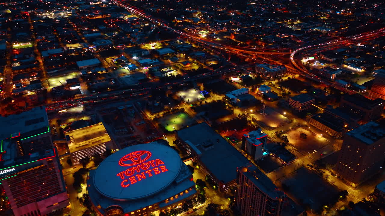 Houston, ABD, 24 Kasım 2025: Houston'daki aydınlatılmış spor arenasının gece kuşbakışı görünümü. Gece Houston şehir merkezinde kırmızı parlayan ışıklara sahip büyük bir kapalı stadyumun yüksek açılı çekimi.