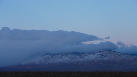 Clouds-rolling-over-a-snowy-mountain-peak-at-sunrise---time-lapse