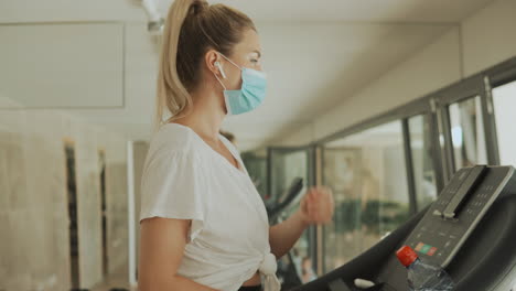 young athlete female with face mask uses an exercise machine and takes a break breathing deep in the gym