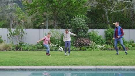 Glücklicher-Kaukasischer-Vater-Mit-Zwei-Söhnen,-Die-Im-Garten-Fußball-Spielen