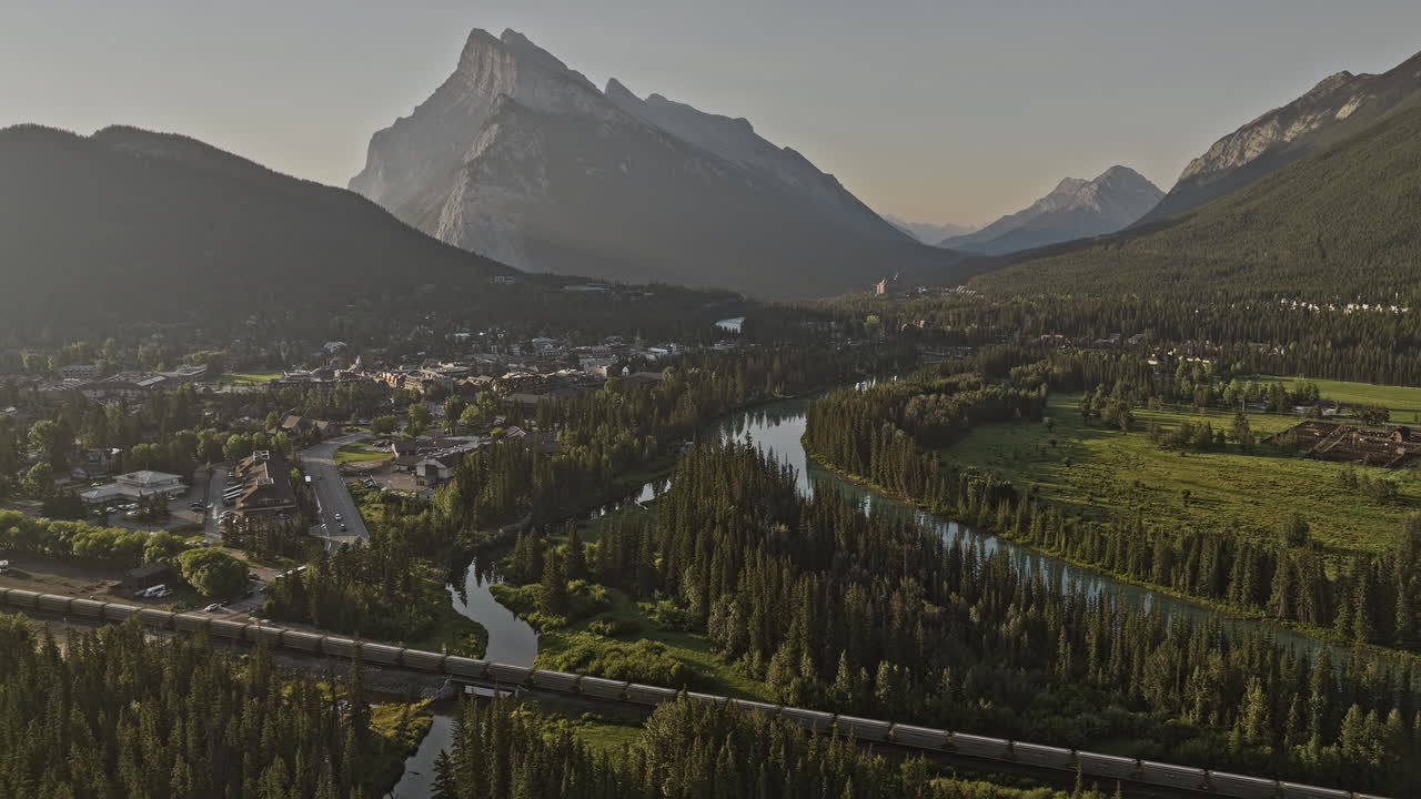 banff ab canada aerial v32 sobrevuelo valle boscoso capturando pintoresca ciudad a lo largo del río bow y vistas de las cadenas montañosas de rundle con tren viajando a través de la escena - filmado con mavic 3 pro cine - julio 2023