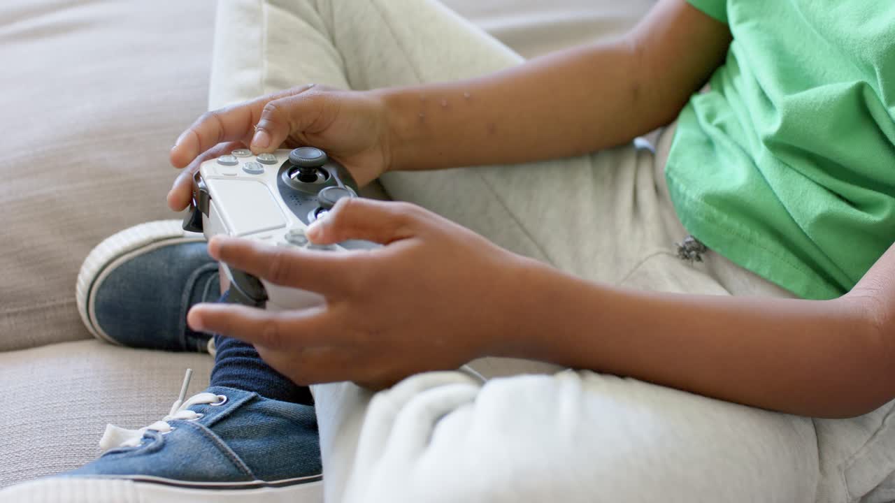 With game starting, child is manipulating white controller on sofa, thumbs pressing buttons to win