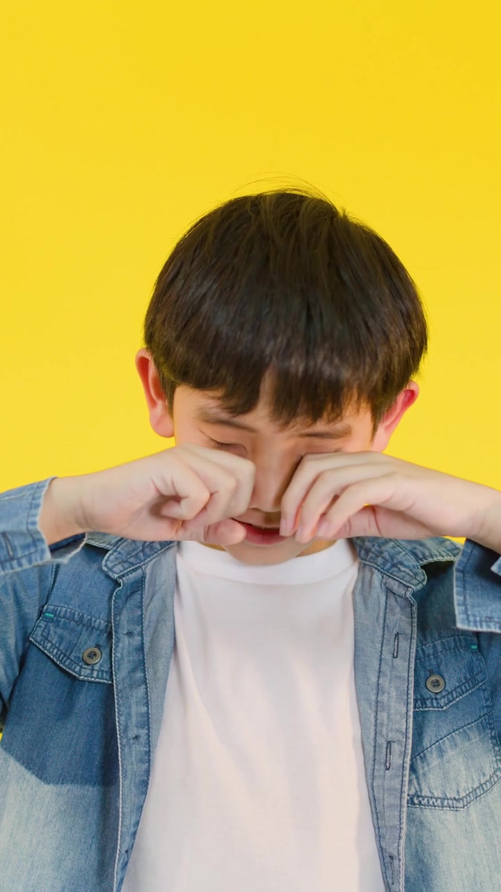 Un ragazzo giovane si strofina gli occhi stanchi, esprimendo sonnolenza, in una luminosa illuminazione da studio con uno sfondo giallo.