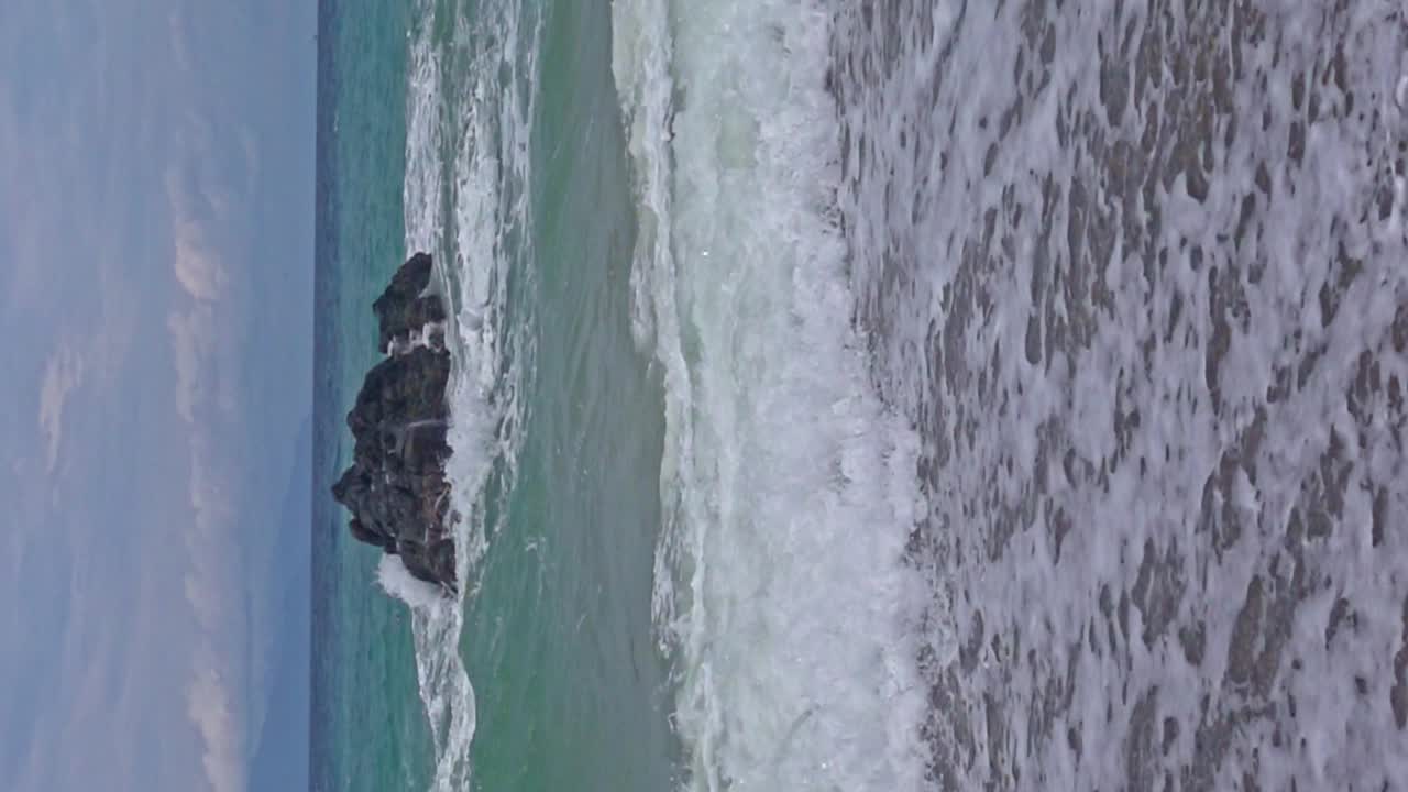 Inquadratura verticale della spiaggia di Banbanon al rallentatore con onde che si infrangono sulla costa sabbiosa