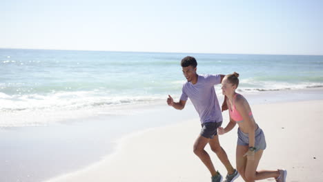 Un-Joven-Birracial-Y-Una-Joven-Caucásica-Están-Corriendo-En-Una-Playa-Soleada-Con-Espacio-Para-Copiar