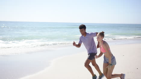a young biracial man and a young caucasian woman are jogging on a sunny beach with copy space