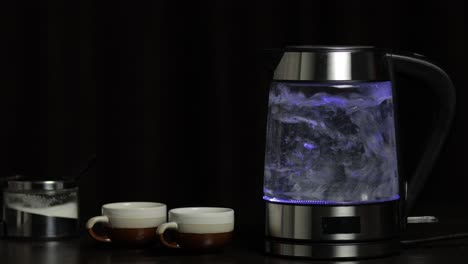 Kochendes-Wasser-In-Einem-Transparenten-Wasserkocher-Aus-Glas-Mit-Blauer-Lichtbeleuchtung.-Schwarzer-Hintergrund