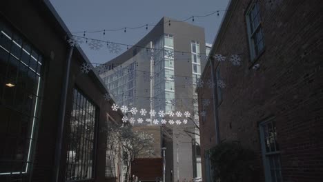 this is a wide shot of a dimly lit alleyway in nashville, adorned with festive snowflake lights, contrasted by the modern building at the end, under an evening sky