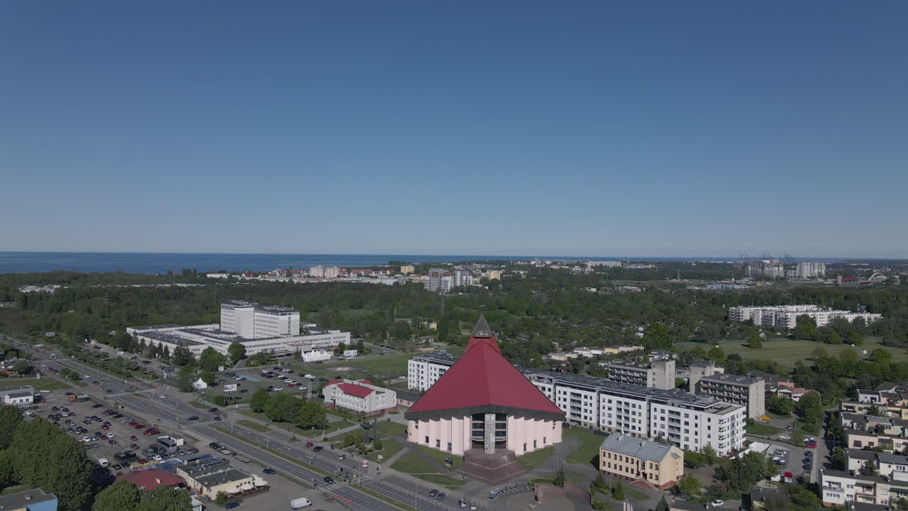 A mighty church with a red roof located near the coast, in the middle of the estate and by the road, drone shot in Gdansk Poland