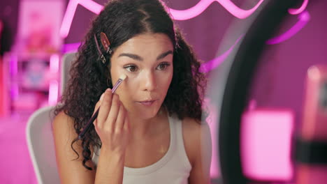 woman applying makeup in front of a ring light