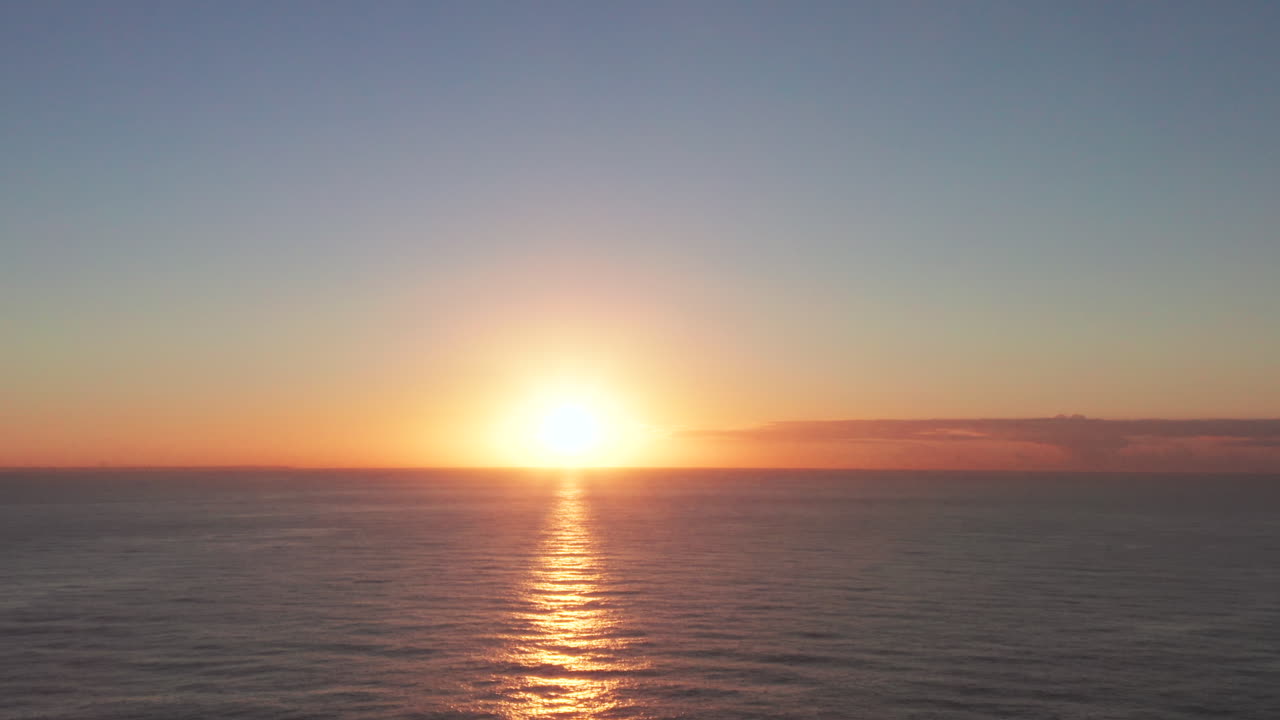 Amazing colorful sky at sunset over sea and silhouette of ship. Aerial forward