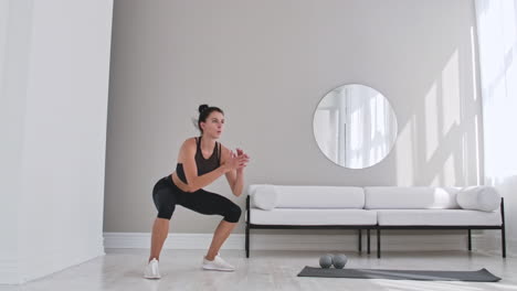 woman exercising jumping squats in home. healthy female in sportswear doing jumping squats at home. woman exercising at living room