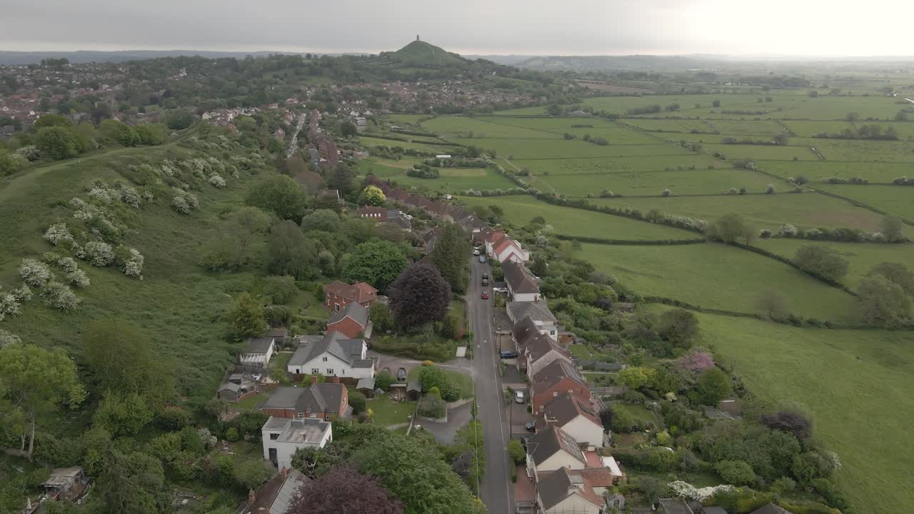 Aerial view of Glastonbury, drone moving forward over the houses and the Main Street leading to the Glastonbury. green fields around the houses . 4K, 60fps.