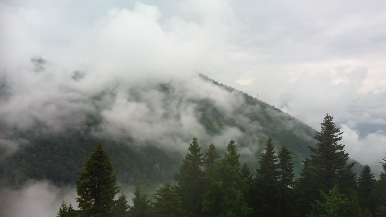 Drone video of a camper van parked on the edge of a mountain with low lying clouds in the valley. Footage moves over the Motorhome to reveal the stunning views behind of the clouds in forest