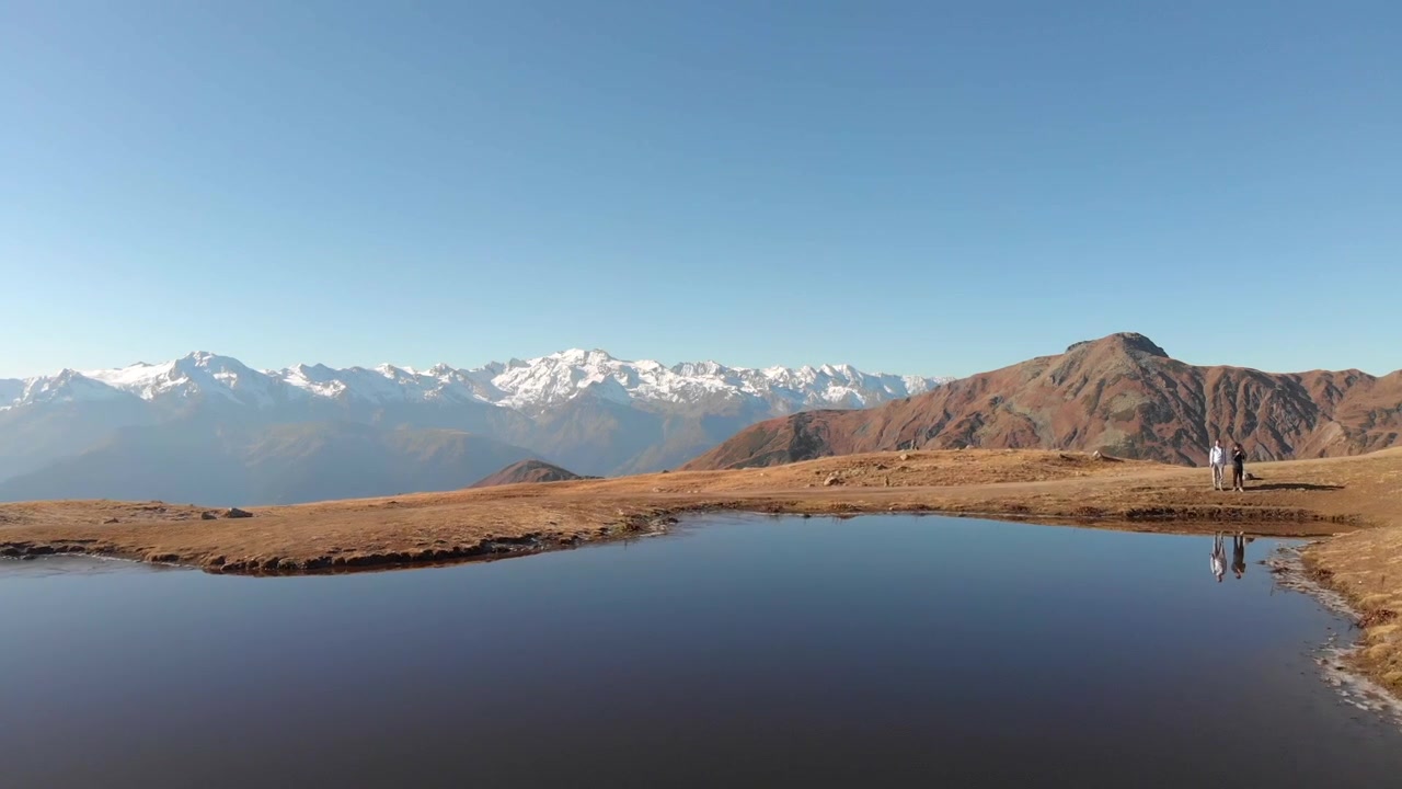 Luchtopname van een schilderachtig Kaukasusgebergte in Georgië, met een klein bergmeer dat de heldere lucht weerspiegelt op de voorgrond.