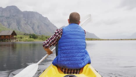 Caucasian-man-having-a-good-time-on-a-trip-to-the-mountains,-kayaking-on-a-lake,-holding-a-paddle