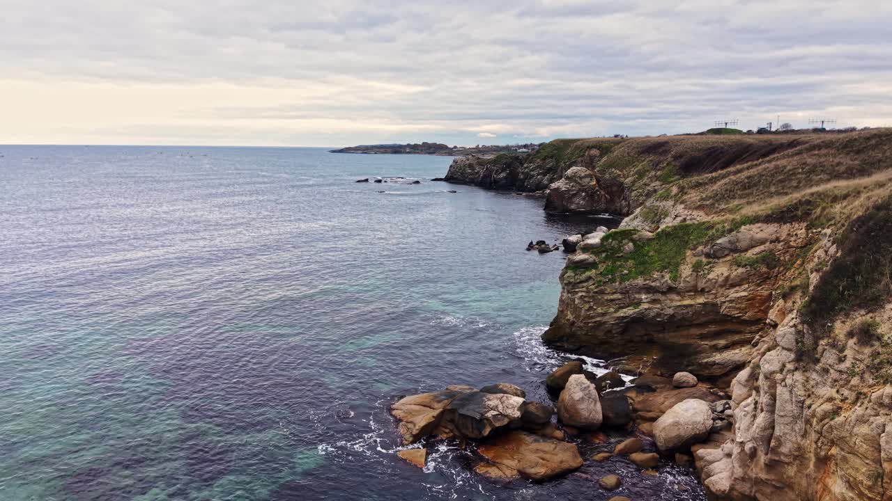 Aerial view of rocky coastline with clear water and soft clouds