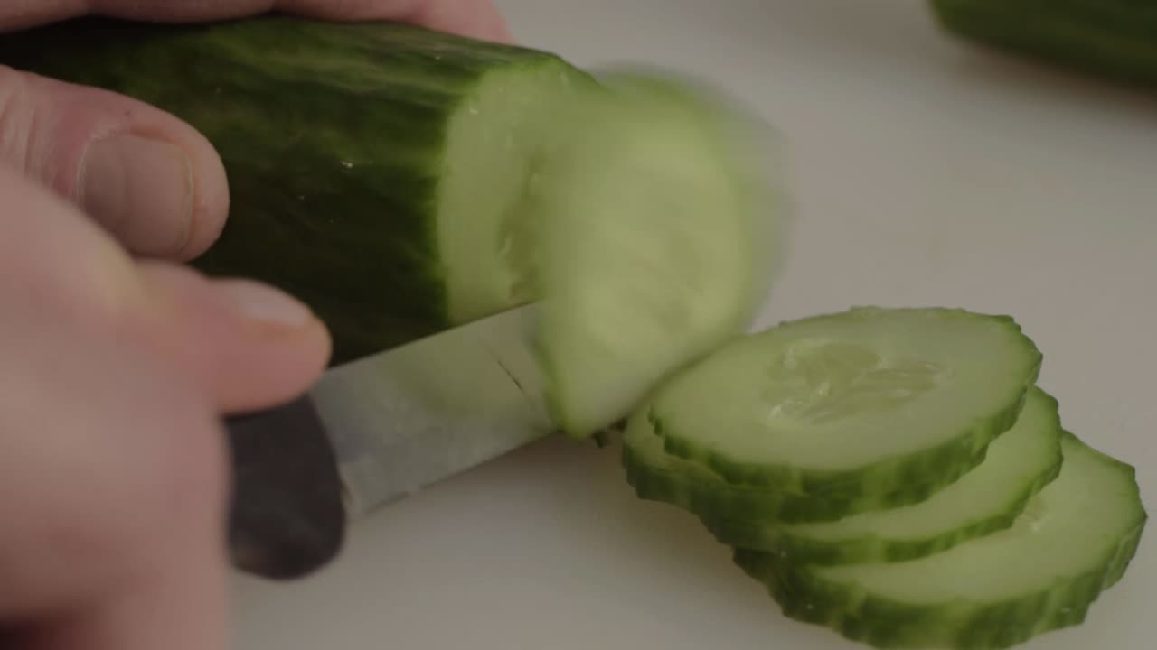 Hand slicing a cucumber with knife close up