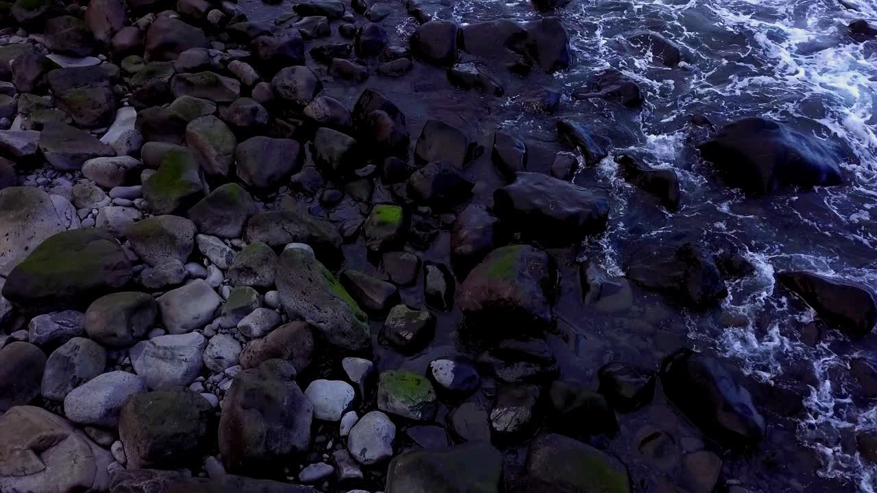 Acqua di mare che scorre su rocce di ciottoli vulcanici neri, asciutti e bagnati; l'onda crea schiuma. Alta marea diurna, vista sull'Oceano Atlantico dall'isola di Madeira, Portogallo. Slow motion HD cine zoom 60fps