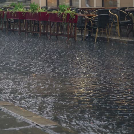stream of water are flowing through the pavement in rainy weather. Raindrops is falling on the road against the background of the summer terrace of the restaurant