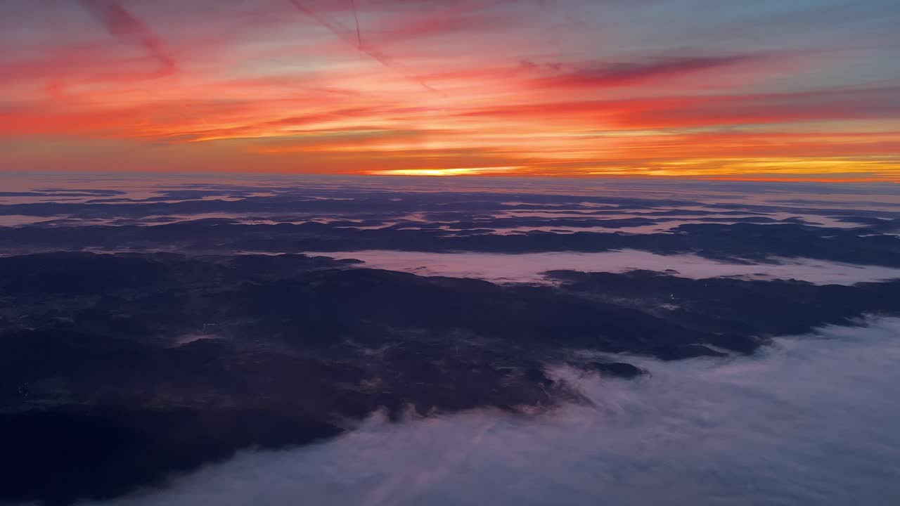 punto de vista piloto único desde una cabina de jet que vuela hacia el sur sobre alemania al amanecer con un cielo naranja intenso y un paisaje brumoso