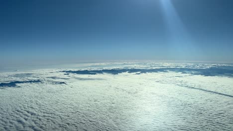 Awesome-aerial-view-from-a-jet-cockpit,-pilot-point-of-view,-flying-at-12000-metres-high-approaching-the-french-italian-Alps-mountains,-with-very-low-clouds-and-a-splendid-blue-sky-with-sunbeams