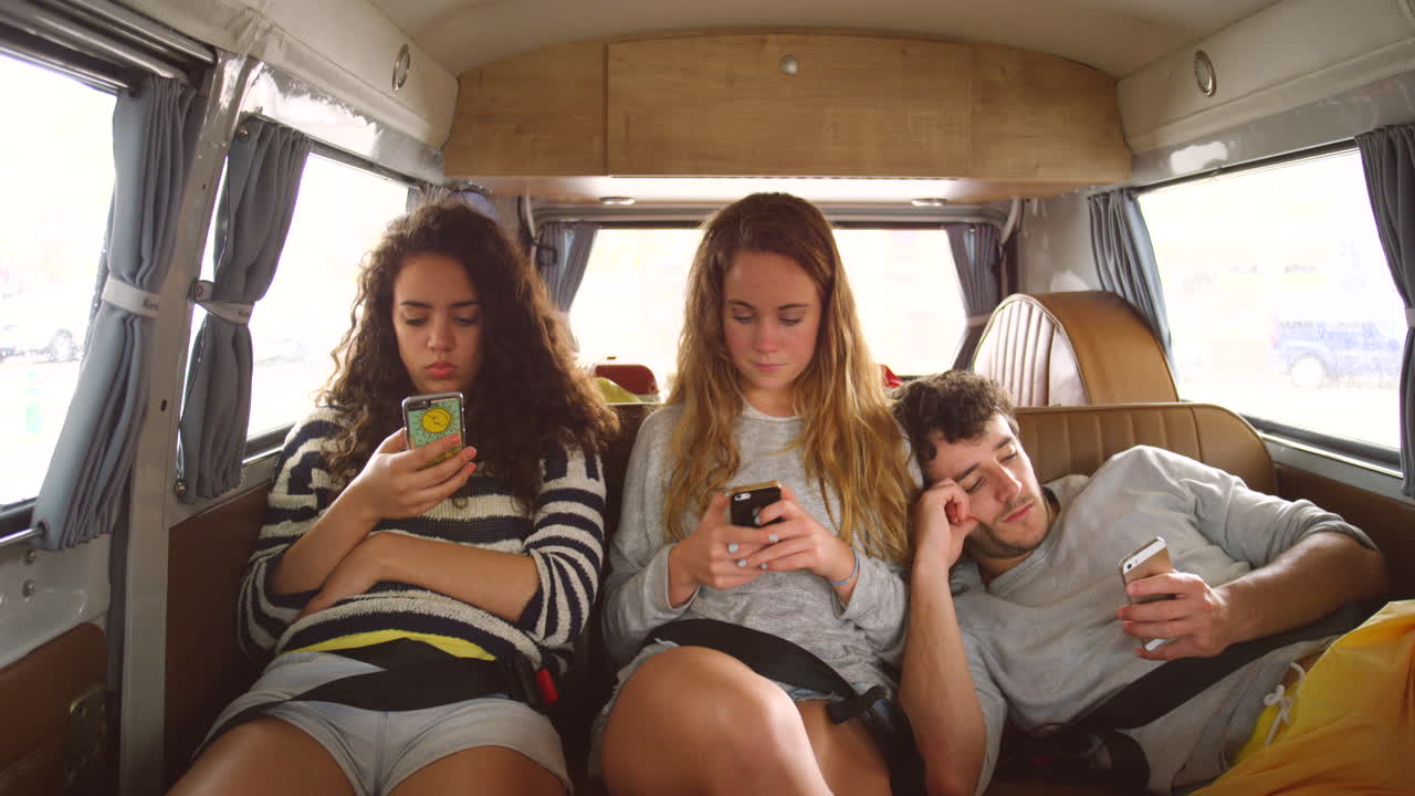 Přátelé na road tripu používající mobilní telefony v dodávce