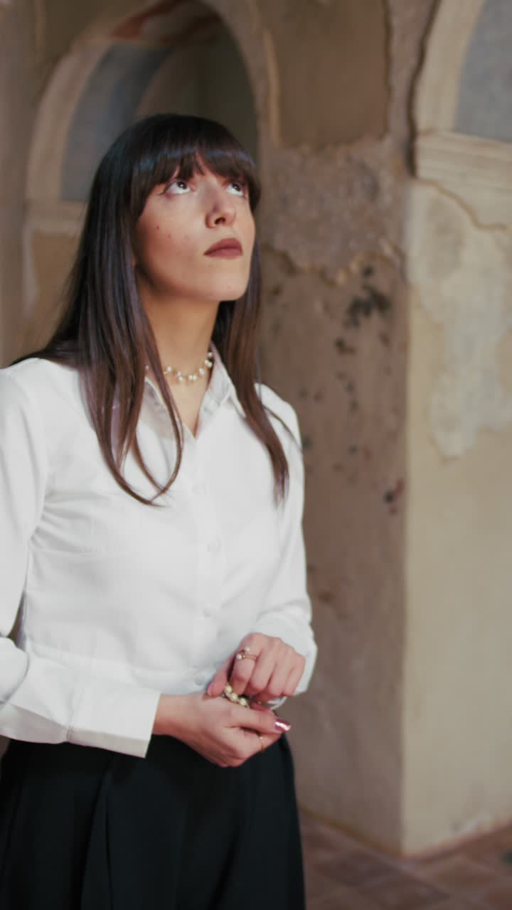 Donna che tiene un rosario in chiesa, ferma e guarda in alto.