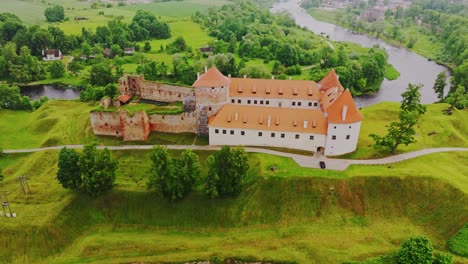 Aerial orbit of Bauska Castle on misty day showing medieval walls and red roofs