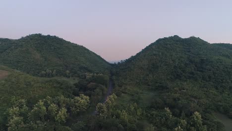 Drohnenaufnahmen-Einer-Einzelnen-Straße,-Die-Bei-Sonnenaufgang-Durch-Zwei-Kleine-Berge-Führt