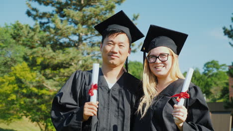 a portrait of two graduates - an asian man and a caucasian woman in the clothes and caps of the grad