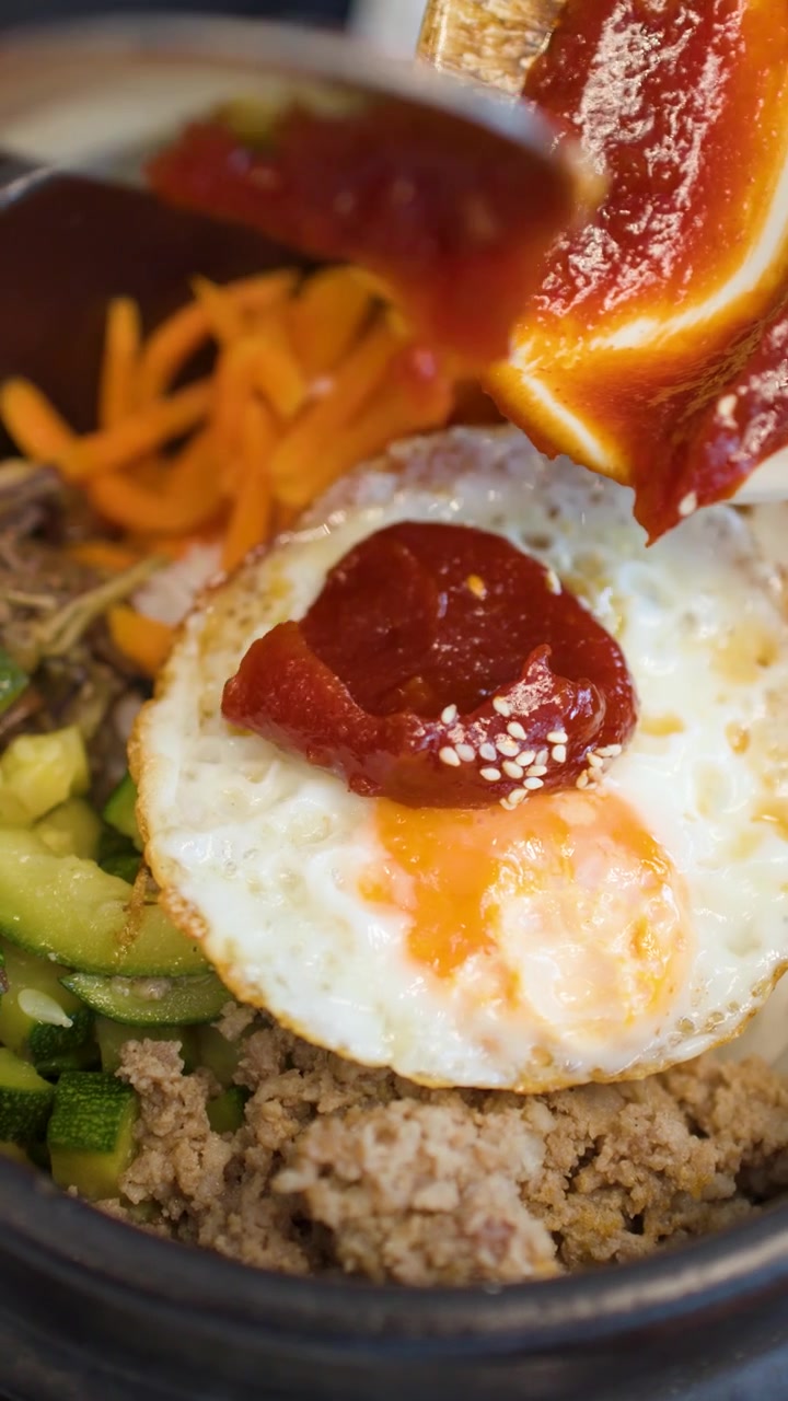 Gambar jarak dekat sambal merah yang dituang di atas nasi, sayuran, dan telur goreng.