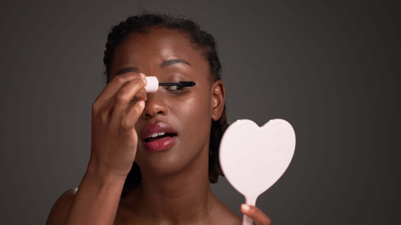 Woman applying mascara with heart-shaped mirror