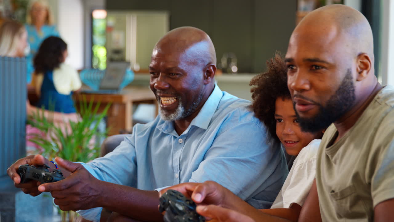 Multi-Generation Male Family Having Fun Playing Computer Game Sitting On Sofa At Home