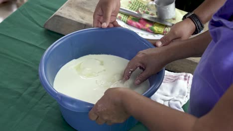 Cheese-Curds-in-blue-bucket-with-Indigenous-woman-from-Costa-Rica-pressing-the-pail-ball,-Close-up-handheld-shot