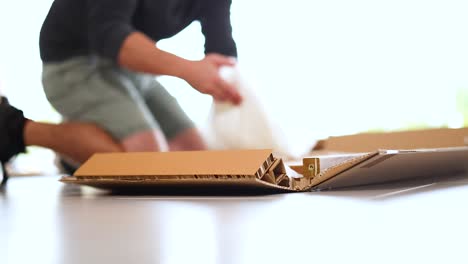 a person unpacks and assembles a wooden item from a box on a table in bright lighting