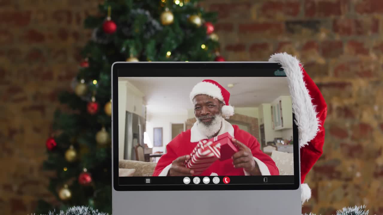 hombre afroamericano senior en disfraz de santa en videollamada en la computadora, con árbol de navidad