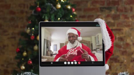 senior african american man in santa costume on video call on computer, with christmas tree