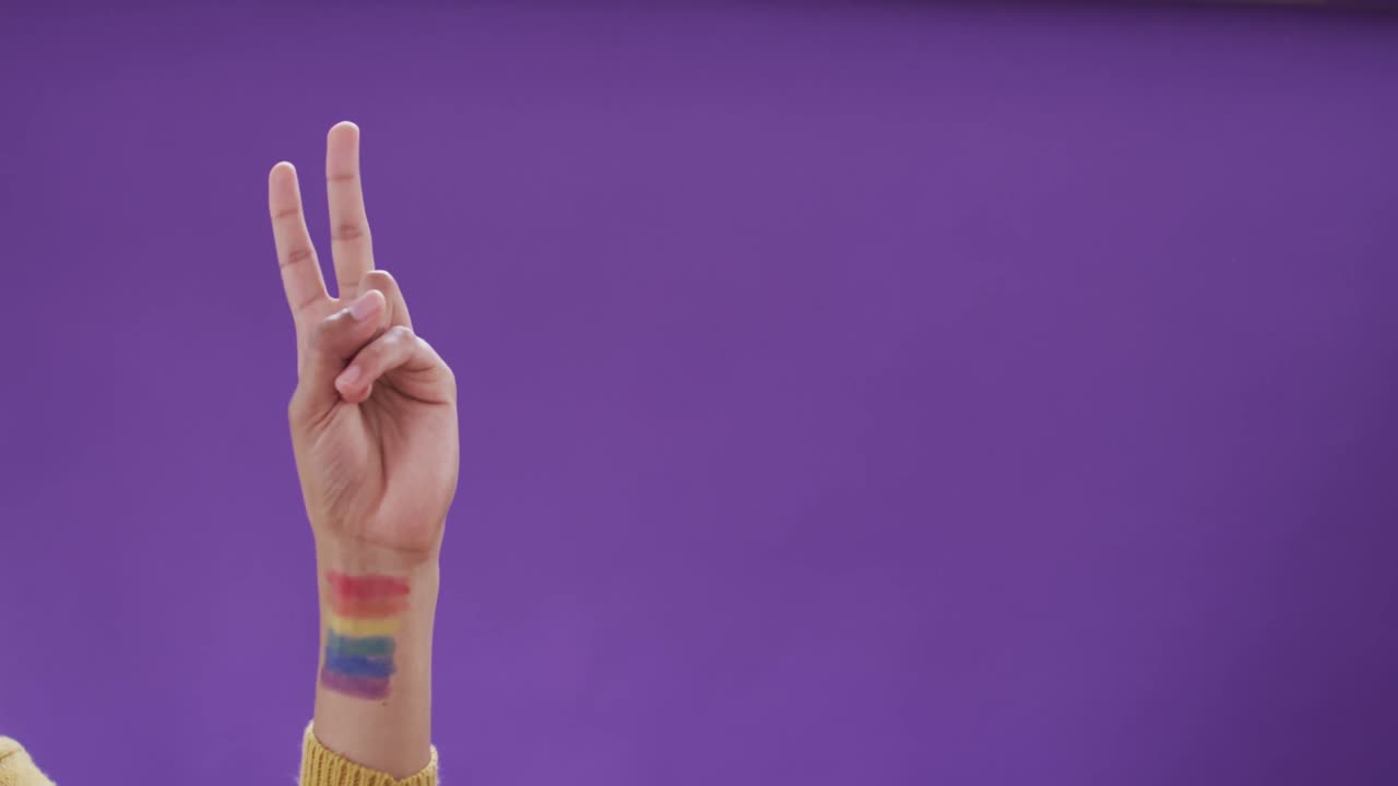 mano de un hombre biracial con bandera lgbt en el brazo sobre fondo púrpura