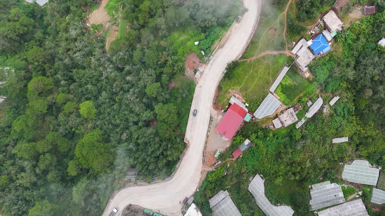 Aerial View of a Winding Mountain Road Through Lush Green Forests and Rural Settlements