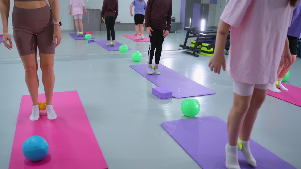 vista parcial de un instructor de fitness dirigiendo a un estudiante en la acumulación de resistencia, usando una pequeña pelota entre sus tobillos, un gran espejo que refleja sus movimientos en un entorno de gimnasio