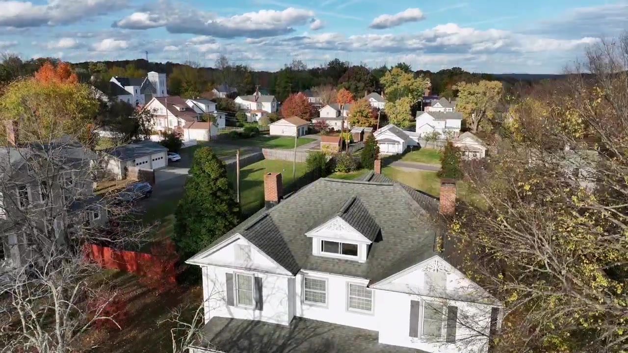 Historic old single Family house with porch in american neighborhood. Quiet residential area in Suburbia with colorful trees during autumn season. red brick chimney on roof. Rising drone wide shot.