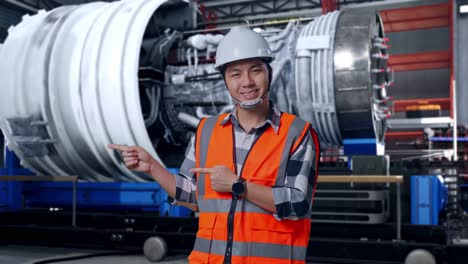 asian male engineer with safety helmet smiling and pointing to side while standing with airplane engine maintenance conducted, analytics checking the turbine