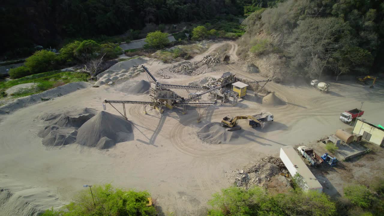 Drone view of heavy machinery working at a cement plant, showing sand piles and conveyors