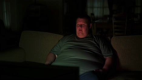 overweight man watching tv on a couch in a dark room