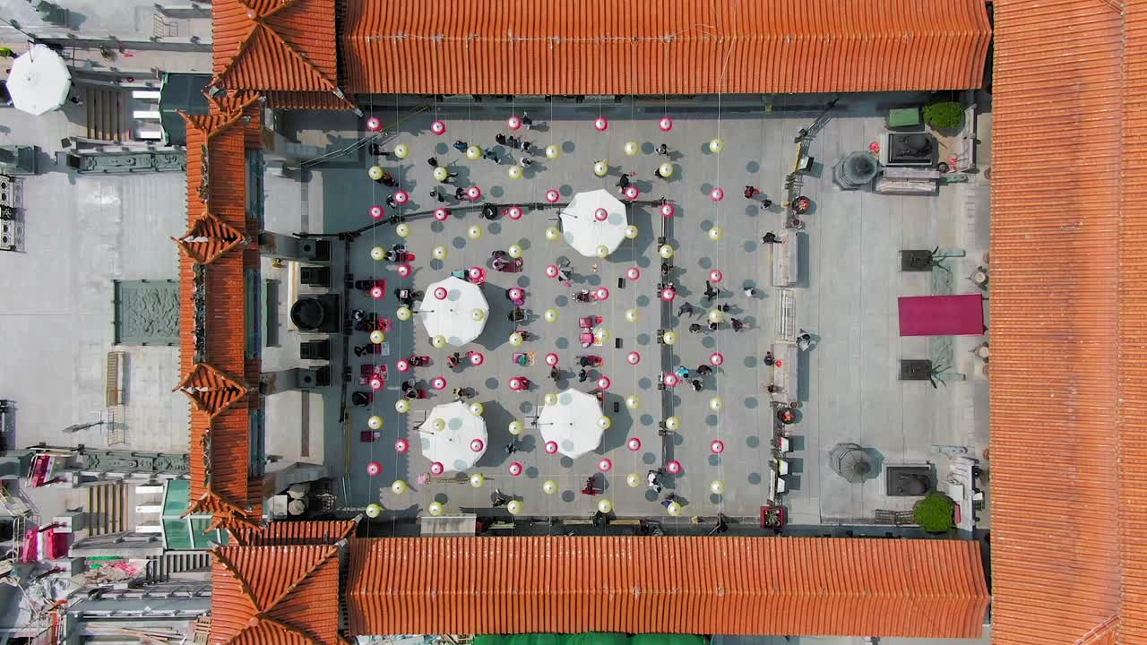 Aerial Time lapse of Wong Tai Sin temple court with people lighting incense sticks and kneel before the main altar under Chinese lanterns.