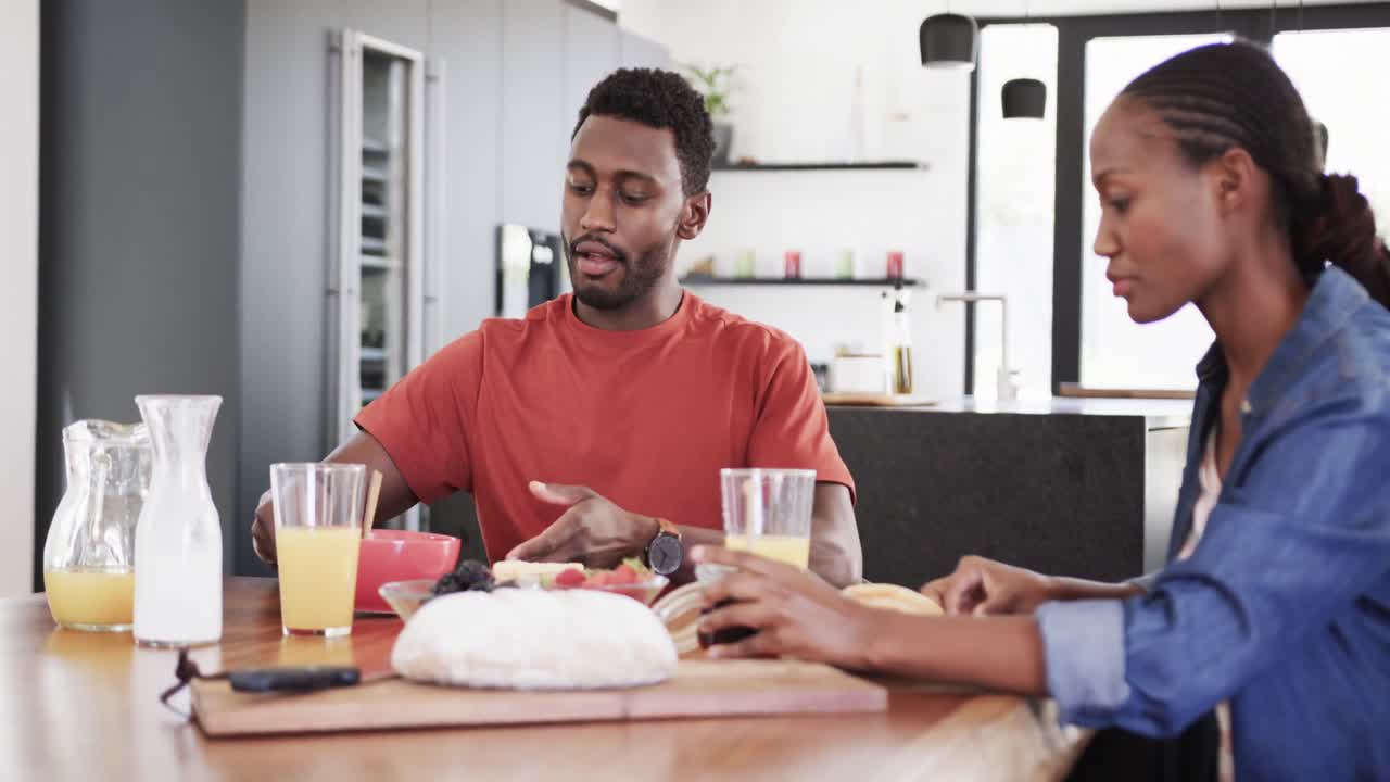 Happy african american couple serving and eating breakfast at table in kitchen, slow motion