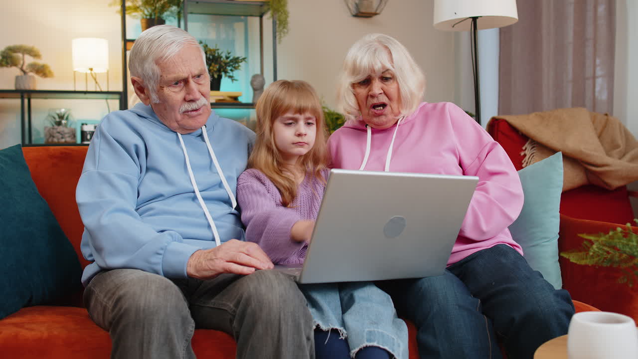 Upset grandfather grandmother and granddaughter playing game on laptop and losing fail at home sofa