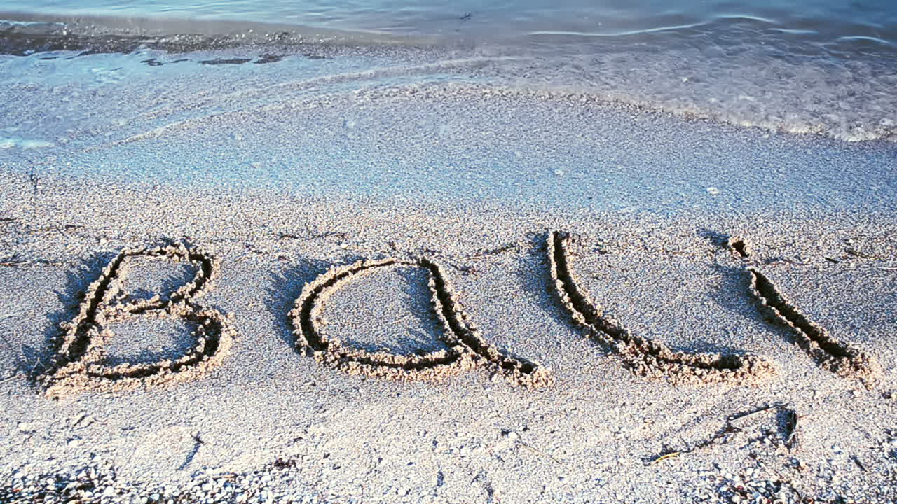 Napis „Bali” na piaszczystej plaży. Napis na piasku, plaża
